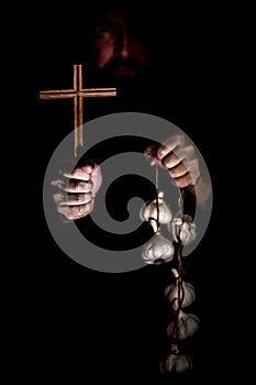Monk in the dark holding a crucifix and a garlic string, vampire cult and their protection photo