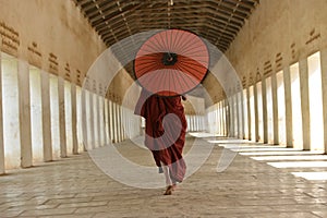 Monk dressred in traditional red outfit with red umbrella in myanmar