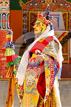 Monk performs a masked and costumed sacred dance of Tibetan Buddhism, another monks play ritual music during the Cham Dance