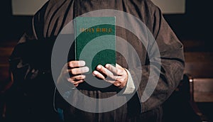 A monk in robes with holy bible in their hands praying in the church