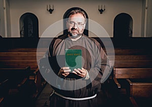 A monk in robes with holy bible in their hands praying in the church