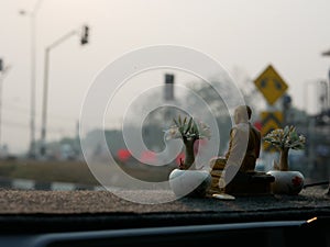 A monk statue being placed on a driving car dashboard as the Thais believe that the statue can save them from road accident