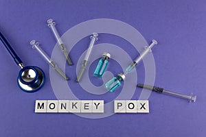 MONKEY POX. Words written on square wooden tiles stethoscope, medicine and vaccine on purple background. photo