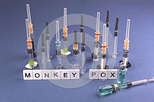 MONKEY POX. Words written on square wooden tiles with vaccine and syringes on blue background. Viral disease. photo