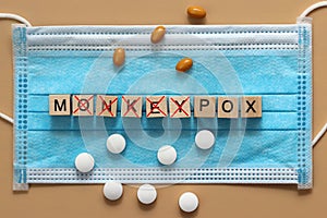 The monkeypox virus is laid out with wooden cubes on a surgical face mask. There are various pills lying around. Renaming the photo