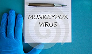 Monkeypox virus symbol. Concept words Monkeypox virus on white note. Doctor hand in blue glove with metallic pen. Medical mask. photo