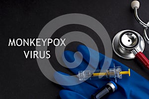 MONKEYPOX VIRUS words written with stethoscope, syringe, glove and vaccine bottle on black background. photo