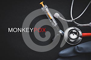 MONKEYPOX words written with stethoscope, syringe, glove and vaccine bottle on black background. photo