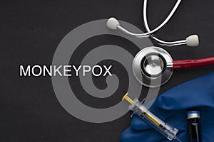 MONKEYPOX words written with stethoscope, syringe, glove and vaccine bottle on black background. photo