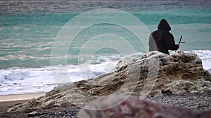 Monks wearing black robes walks on the beach with woden stick in hands at morning. Unrecognizable persone, slow motion.