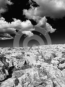 Monochome surreal image of a harsh rocky landscape in bright light with dark contrasting sky and white clouds