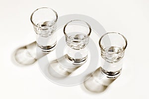 Monochromatic image of three empty shot glasses, harsh side lighted with hard shadows. High angle view