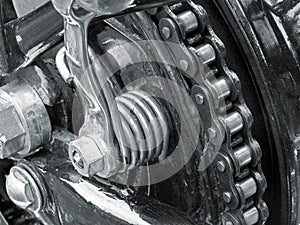 Monochrome close up of the drive chain on a black vintage motorbike with chrome fixtures and steel bolts