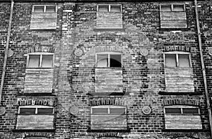 Monochrome derelict abandoned old brick industrial building with red painted broken boarded up decaying windows