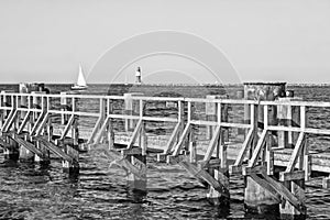 Monochrome image of the Baltic Sea with wooden pier, lighthouse and sailing ship at Rostock Warnemuende, Germany photo