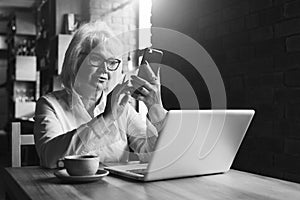 Monochrome image. Businesswoman is sitting at table in front of laptop and using smartphone.Education for adults