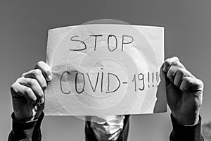 Monochrome image of a desperate teenage boy wearing surgical mask holding a message in isolation