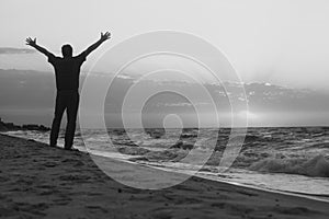 Monochrome image. Man welcomes the sunrise on beach