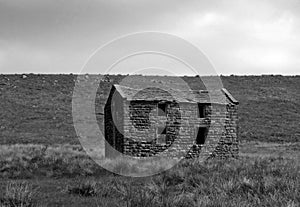 Monochrome image of a an old abandoned stone farmhouse in green pasture on high moorland with cloudy overcast sky