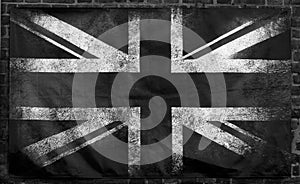 Monochrome image of an old stained dirty union jack british flag with dark crumpled edges on a brick wall background