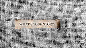 Monochrome image of a rough linen fabric with a torn window in the middle with a Whats your story? sign in it