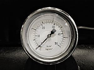 monochrome image of a round shiny pressurevintage gauge with numbers marked in psi and metric on the meter dial on industrial