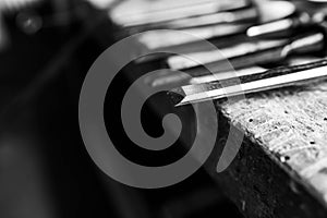 Monochrome image, sharp chisels in row on aged old oak wood workbench, shallow depth of field