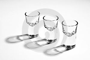 Monochrome image of three empty shot glasses, back lighted, hard reflections