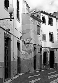 monochrome image of a typical quiet empty street in funchal madeira with old traditional houses painted in faded peeling paint and