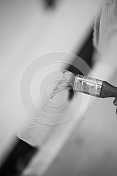 Monochrome image of using a paintbrush to varnish a wooden fence