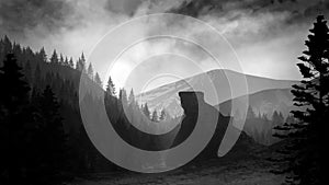 A monochrome mountain landscape, a scene with thick clouds and a bright sun at sunset or dawn. Gray background with a stone upland