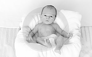 Monochrome photo of little baby lying on big cushion