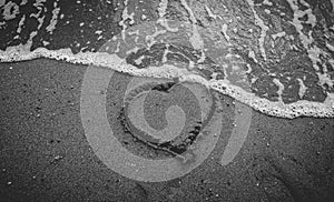 Monochrome photo of sea wave washing away heart drawn on sand