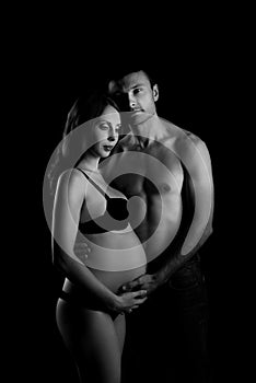 Monochrome portrait of happy loving couple in a moment of love and tenderness. Pregnant woman with hands over tummy.