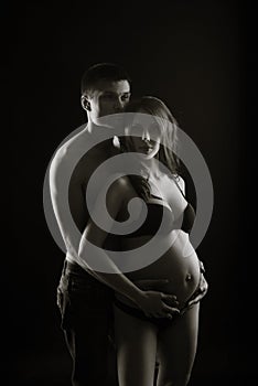Monochrome portrait of happy loving couple in a moment of love and tenderness. Pregnant woman with hands over tummy.