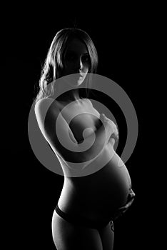 Monochrome portrait of happy pregnant woman with hands over tummy. Black and white photo.