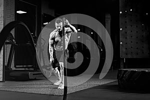 Monochrome portrait of shirtless man training with ropes.
