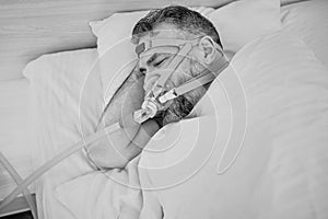 Monochrome portrait of Sleeping man with chronic breathing issues considers using CPAP machine in bed.