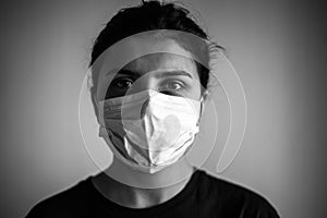 Monochrome portrait of a young woman wearing medical mask. Dramatic black and white closeup of a girl being protected from