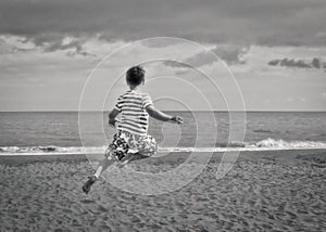 Monochrome shot of a boy from behind jumping near the sandy beach at Stone Bay in Broadstairs