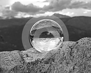 Monochrome shot of a crystal ball put on a rock with a reflection of mountains in the background