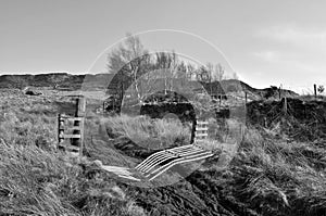 Monochrome view of high pennine farmland with a broken gate across a pathway leading to midgley moor in calderdale west yorkshire