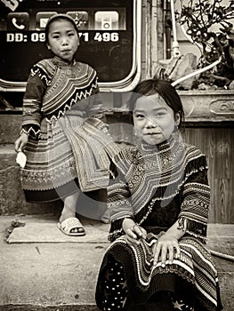 Monochrome - 2 Young minority tribe girls sit outside of mobile phone shop.