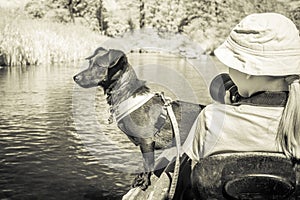 Monochromic view of a dog and a young girl, wearing a hat, in a kayak