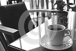 Monotone image of a cup of coffee on a table with empty chair