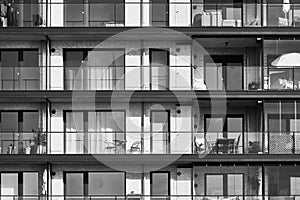 Monotonous balconies and terraces with tables and chairs in a big boring apartment building with big windows, black and white