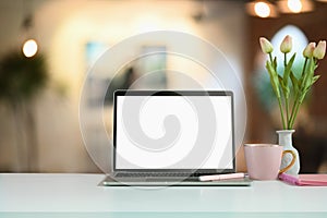 Montage computer laptop with a white screen is putting on a counter bar with a tulips jar and coffee cup.