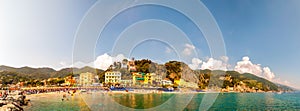 Panorama of rocky marina, clear water of Ligurian Sea, sea ships, beach full of people, waterfront buildings in Monterosso Al Mare