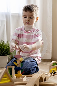 Montessori material. Boy builds a wooden railroad on the floor. Imaginary world of childhood