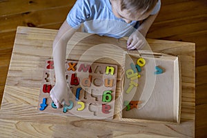 Montessori material. Cute little boy playing with wooden letters alphabet. Study of literacy. Flat lay